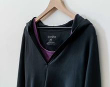 Load image into Gallery viewer, An amrêve organic black pima cotton hoodie is hanging on a wooden hangar. The amrêve purple cotton bra is under the hoodie.