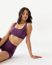 Load image into Gallery viewer, A woman in amrêve organic purple bralette and lounge short is sitting on the floor and leaning on one arm.
