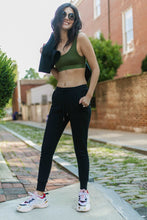 Load image into Gallery viewer, Photo of a woman wearing amrêve organic pima cotton joggers in black and organic pima cotton bralette in chive.
