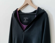 Load image into Gallery viewer, An amrêve organic black pima cotton hoodie is hanging on a wooden hangar. The amrêve  purple cotton bra is under the hoodie.
