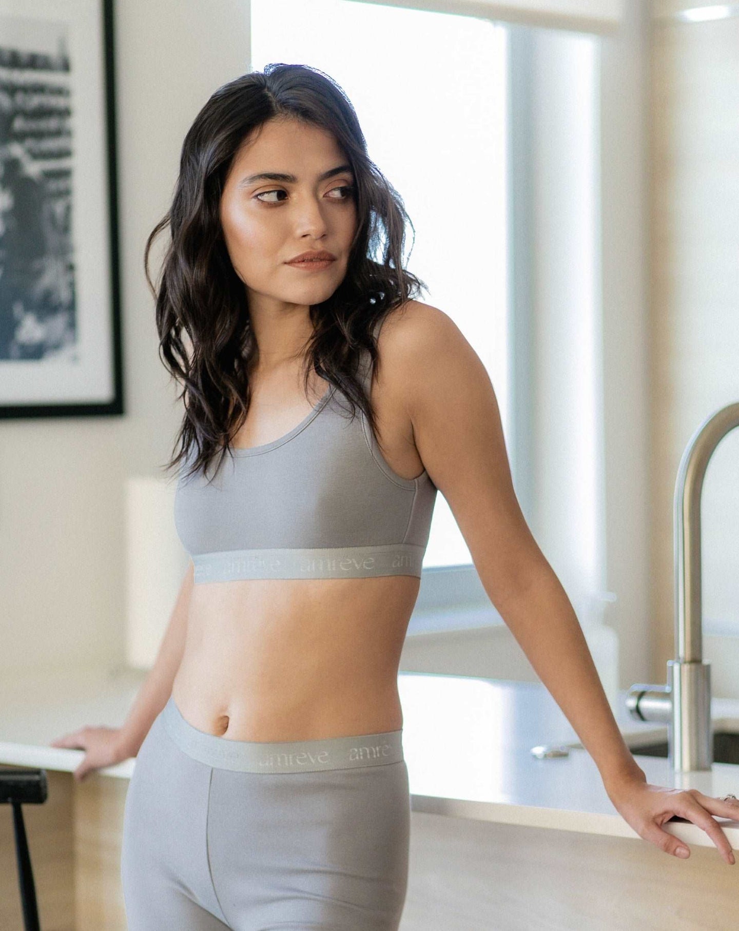 Photo of a woman wearing amrêve organic pima cotton bralette and bike shorts in grey leaning on the kitchen counter.