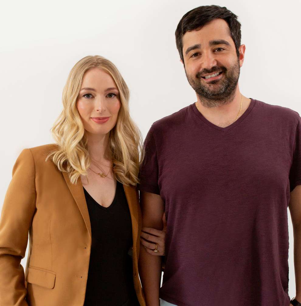 Photo of amrêve founders Nicole and Dany in front of a white backdrop. Nicole is wearing a black v-neck shirt and tan blazer and Dany is wearing a purple shirt. They are smiling looking at the camera.