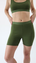 Load and play video in Gallery viewer, Video of a woman wearing amrêve organic pima cotton bike shorts and bralette in chive green. She turns to the side, to the back, and to the side to show the seamless lines of the bike shorts.
