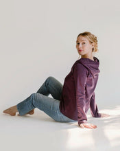 Load image into Gallery viewer, A woman is sitting on the ground wearing jeans and the amrêve purple organic hoodie.
