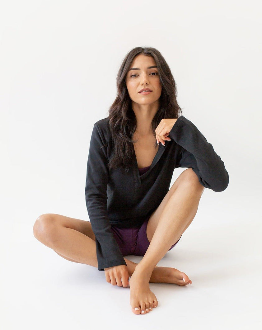 A woman wearing the amrêve black organic cotton hoodie over the amrêve bralette and shorts. She is sitting on the ground.